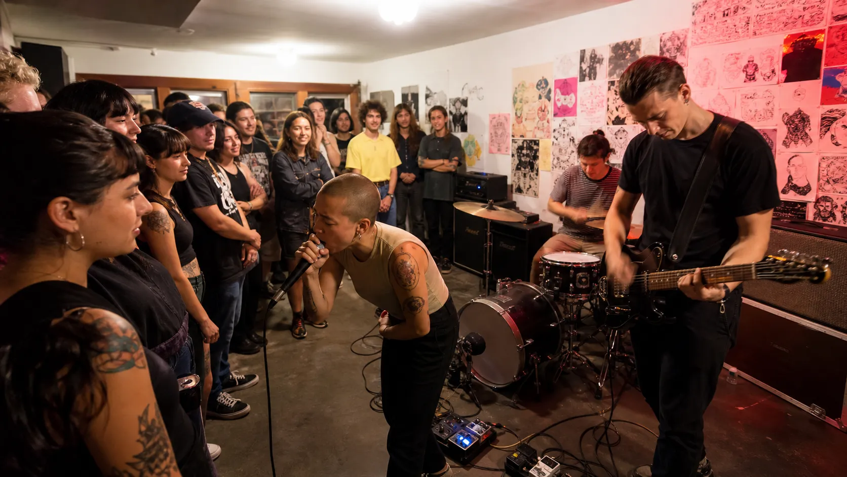 An anonymous punk group performs at floor level in a small community room surrounded by a close audience.